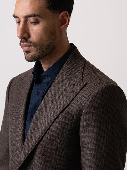 Close-up of the wide peak lapel on a deep brown houndstooth blazer — bold framing, textured weave, and sharp tailoring that defines presence without noise.