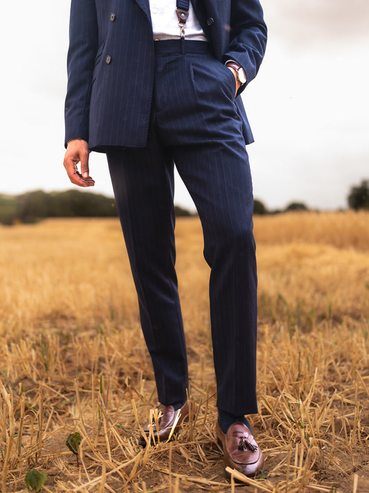 Front view of chalk stripe Gurkha trousers against a backdrop of golden grass. Crisp lines, textured fabric, and timeless tailoring in natural light.