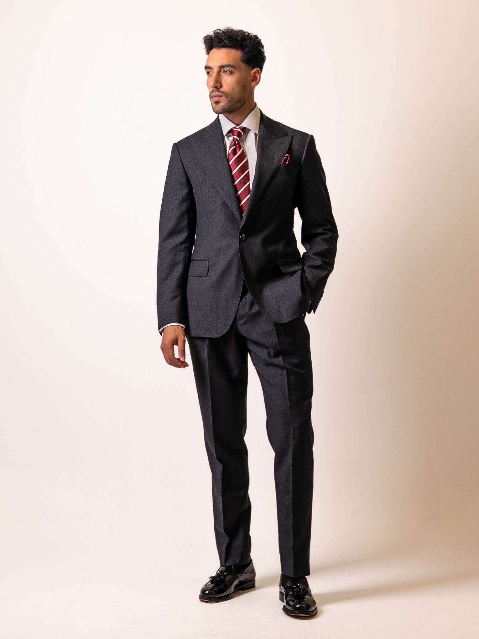 A man stands with hand in the flap pocket of his made-to-measure dark sharkskin grey suit