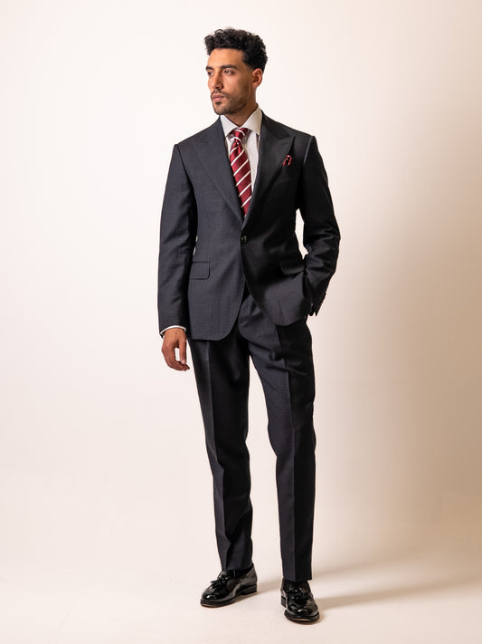 A man stands with hand in the flap pocket of his made-to-measure dark sharkskin grey suit