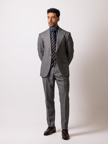 A man in a made-to-measure light grey houndstooth suit stands with hands clasped behind his back
