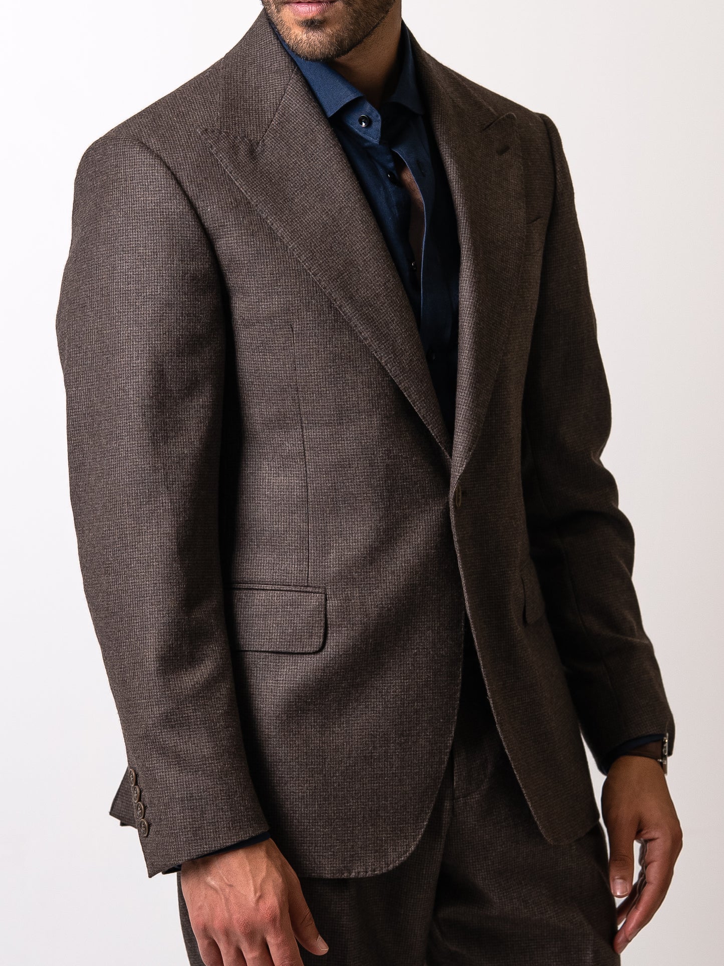 Close-up of functional cuff buttons on a tailored deep brown houndstooth blazer as the man rests his hand in the flap pocket 