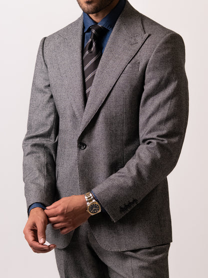 Slightly angled front view of the tailored light grey houndstooth suit as the man holds his right sleeve