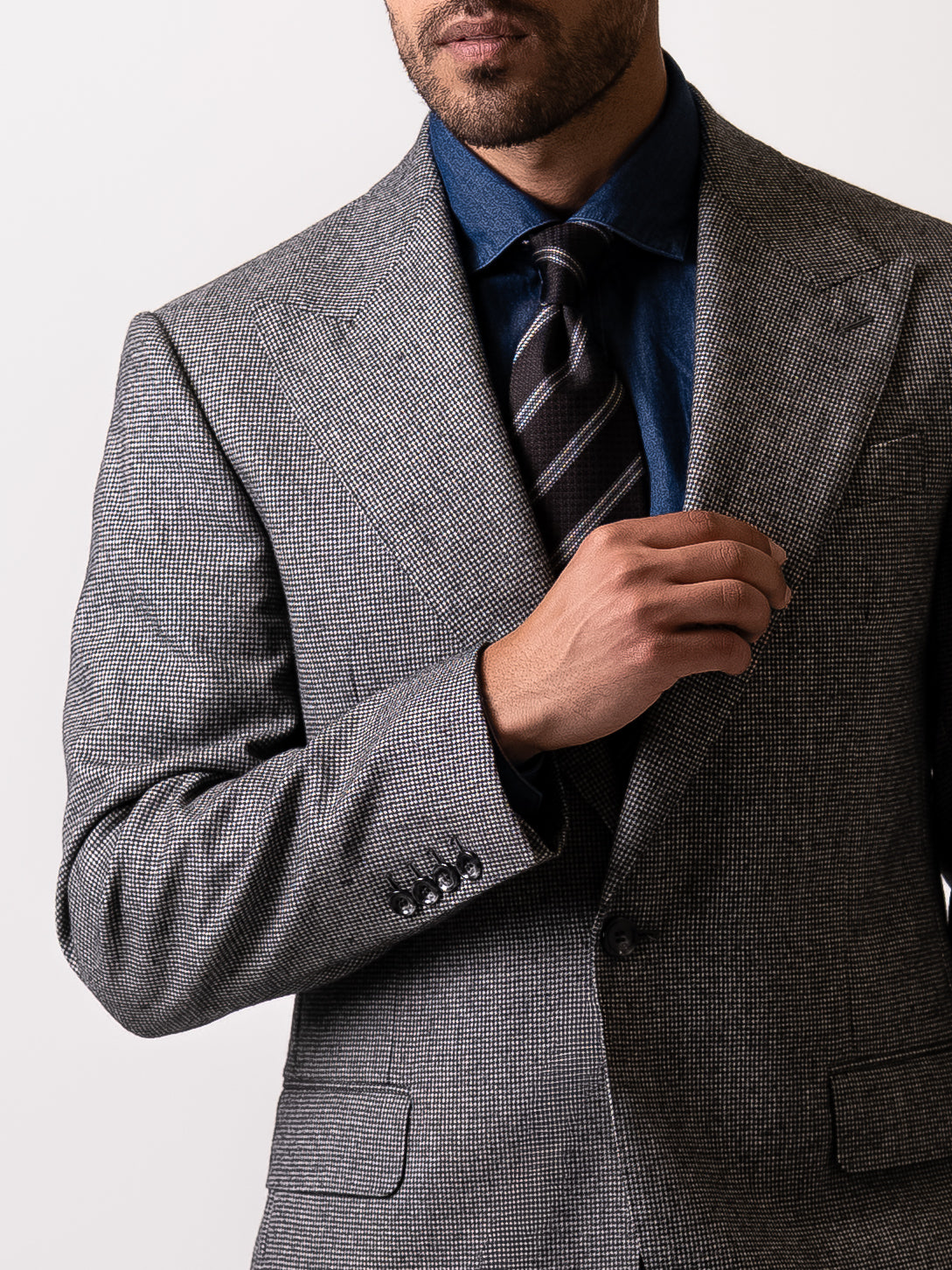 Close-up of the wide peak lapel on a tailored light grey houndstooth blazer.
