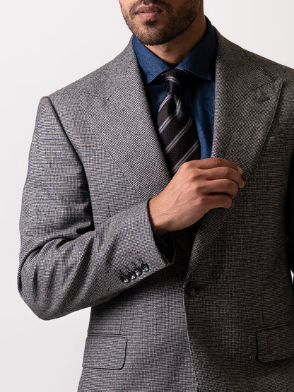 Close-up of the wide peak lapel on a tailored light grey houndstooth blazer.