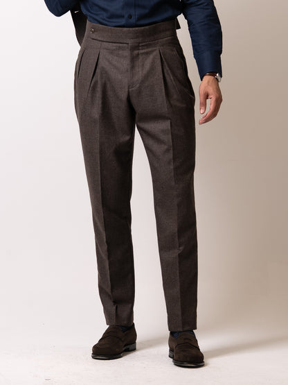 A man in deep tailored brown houndstooth trousers. Double pleats, side fasteners, and a clean belt-free waist 