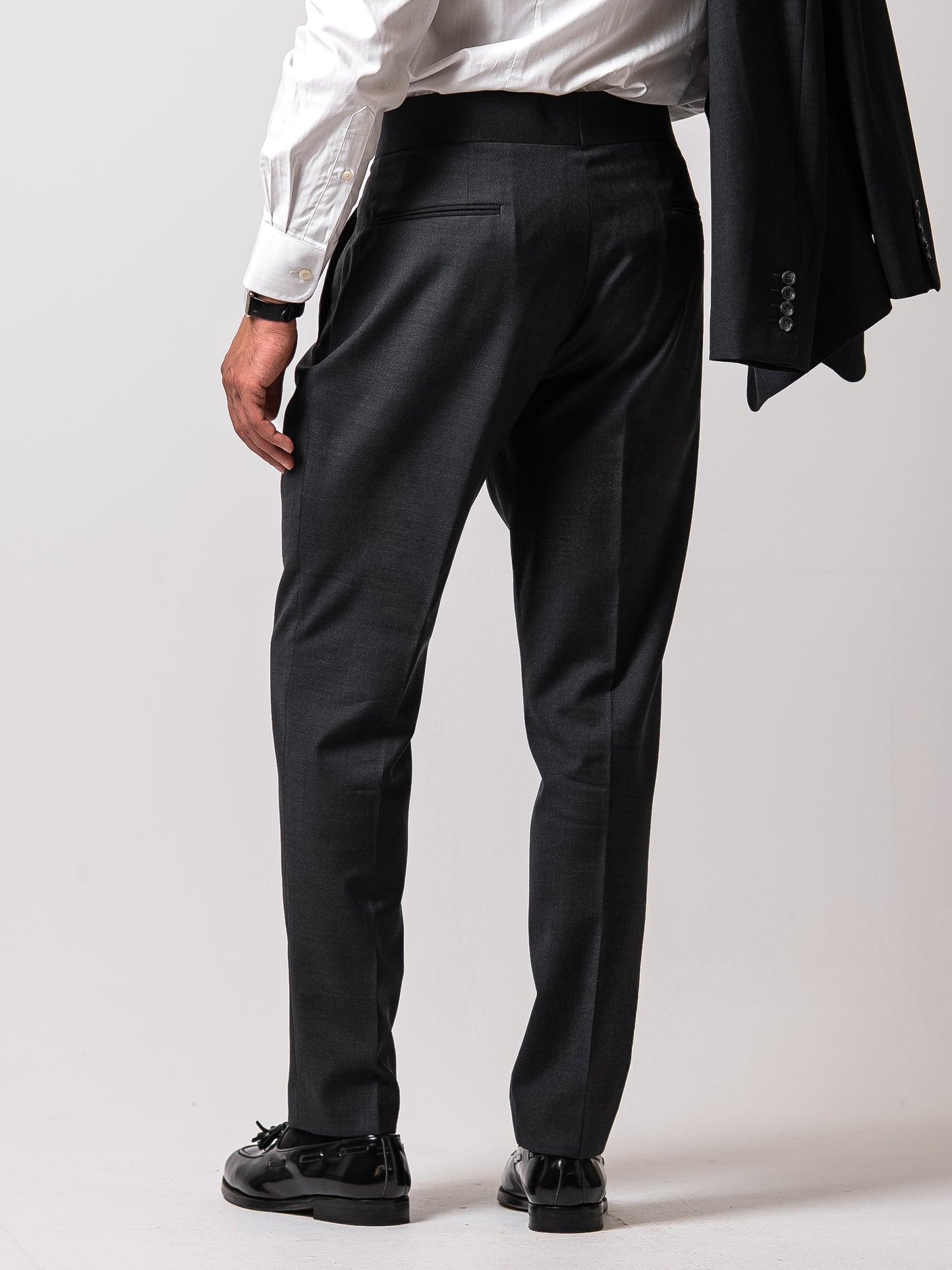 Back view of made-to-measure dark sharkskin grey trousers. Showcasing the refined back pocket, double pleats, and uninterrupted silhouette of Aster Legacy’s Gurkha-inspired cut.