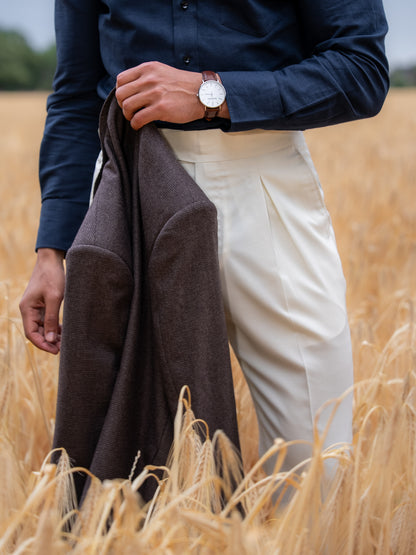 A man walks through soft daylight holding his blazer, white trousers flowing with each step