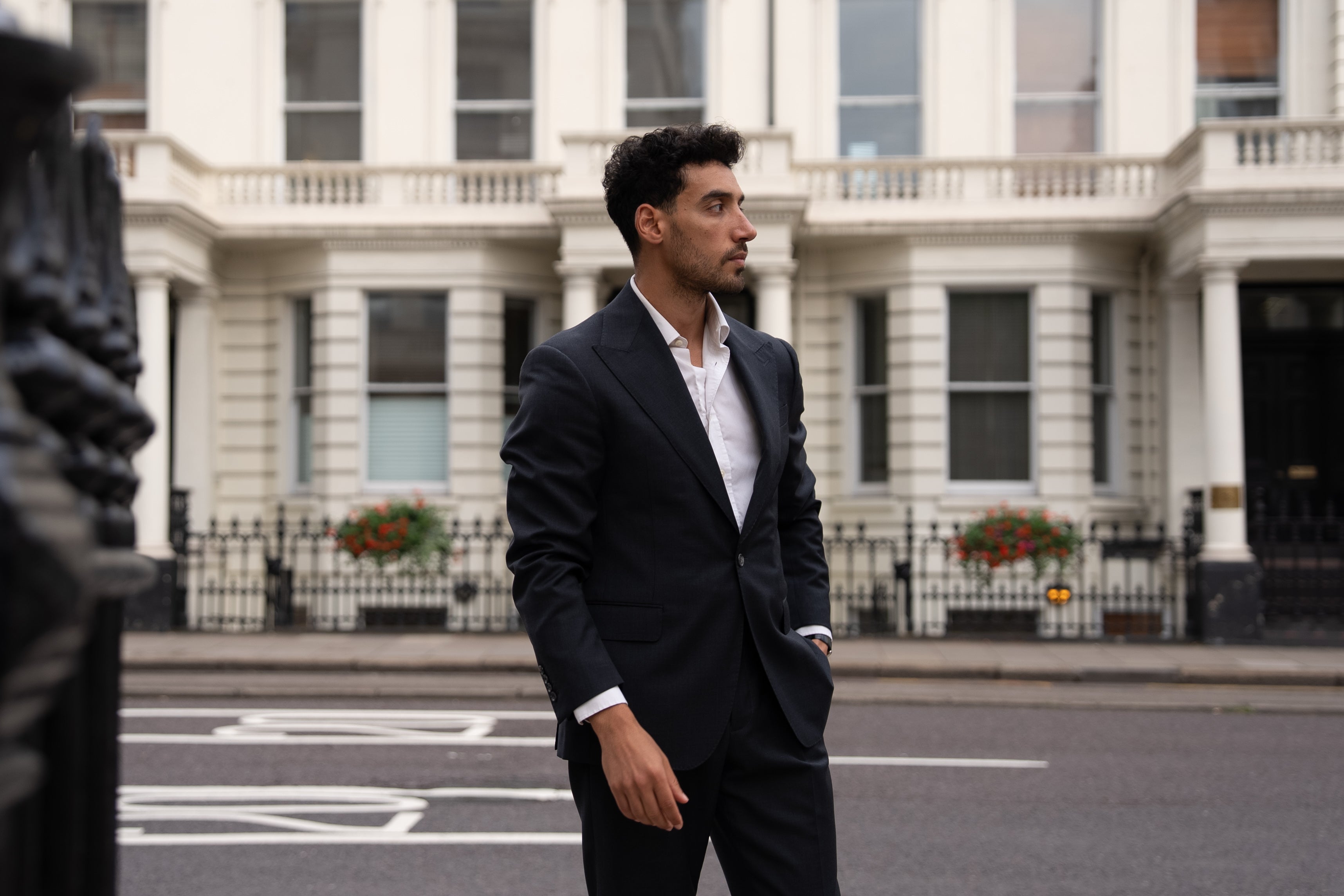 A gentleman in a dark grey sharkskin suit walks through a sunlit London street at dawn. Clean lines, subtle texture, and timeless presence in motion.
