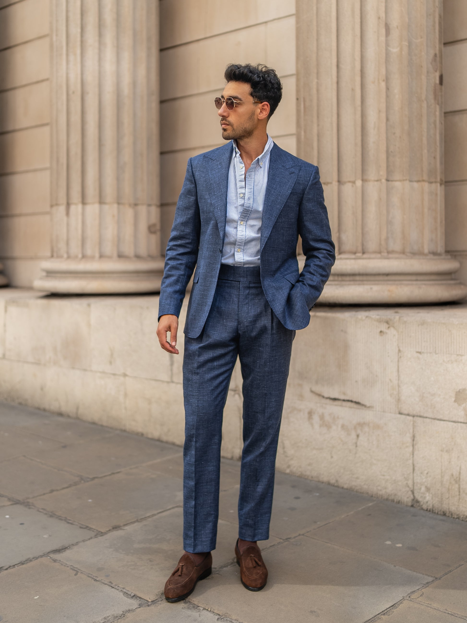 A man in a made-to-measure light blue linen-wool suit wears sunglasses while walking through a London street