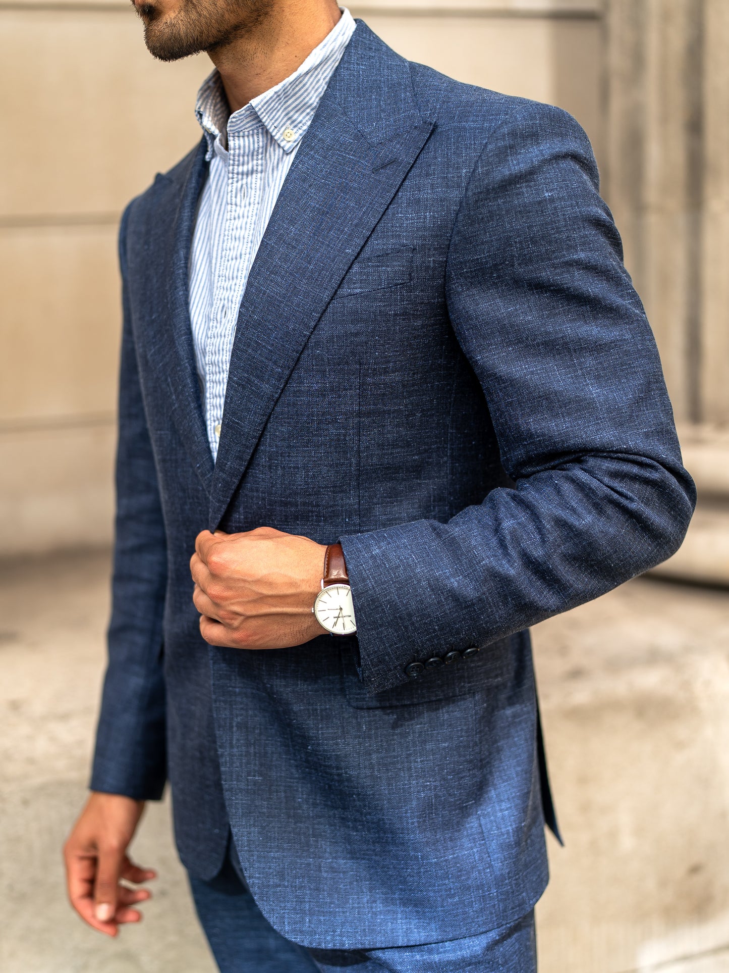 A man gently holds the single-button closure of his tailored light blue linen-wool blazer