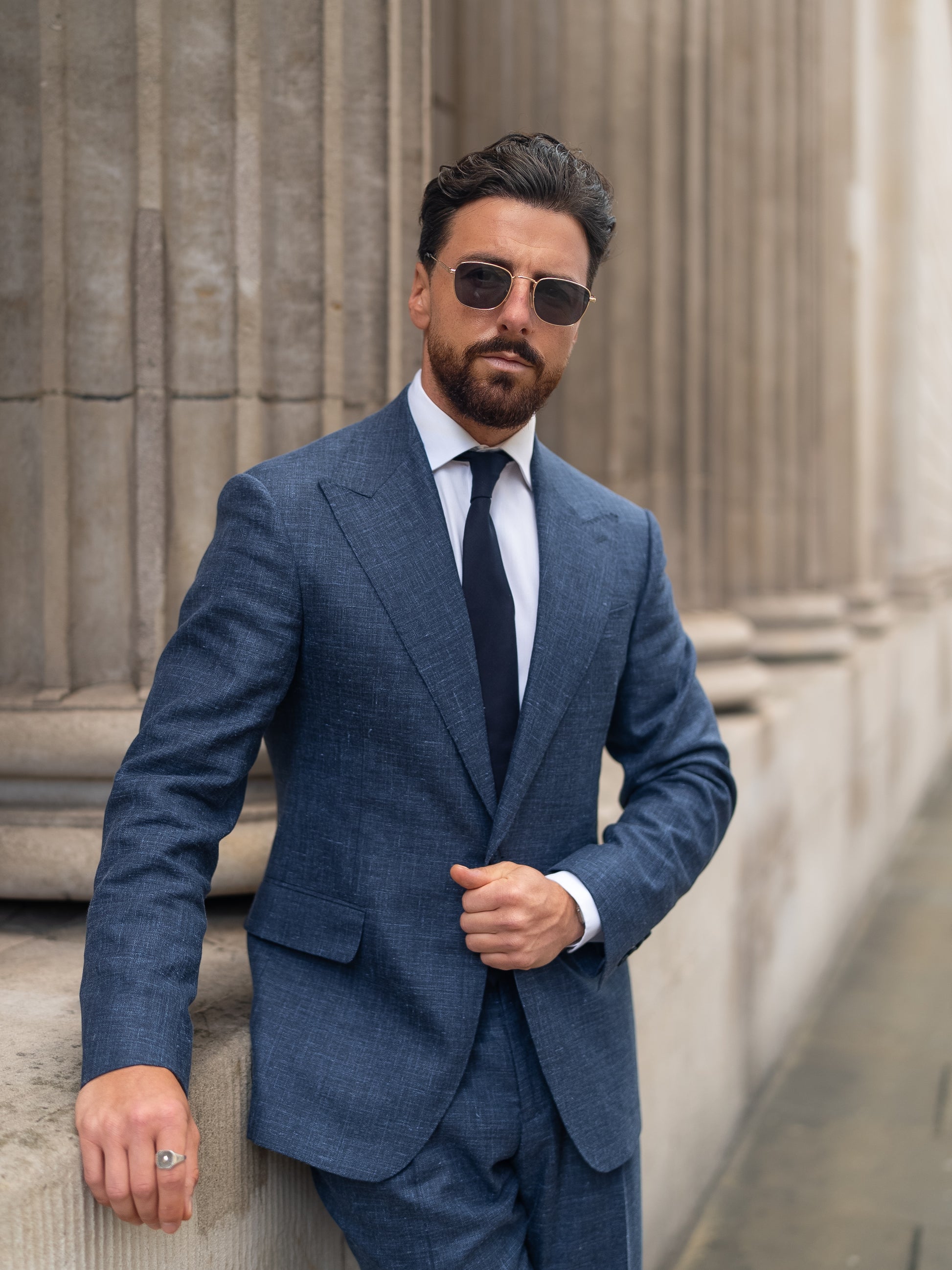 A man in a tailored light blue linen-wool blazer wears sunglasses