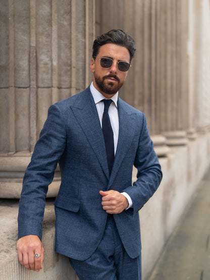 A man in a tailored light blue linen-wool blazer wears sunglasses