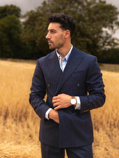 A man holds his chalk stripe double-breasted blazer in front of a golden wheat field. Heritage texture meets open-air calm, where tradition breathes freely. 