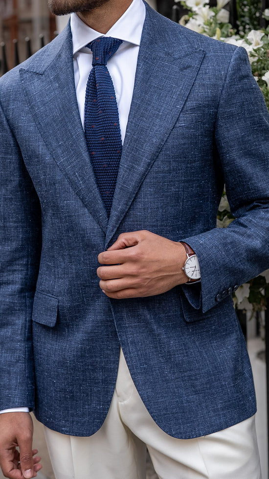A man in a made-to-measure light blue linen-wool blend blazer with a relaxed yet structured silhouette, standing in soft daylight. 

