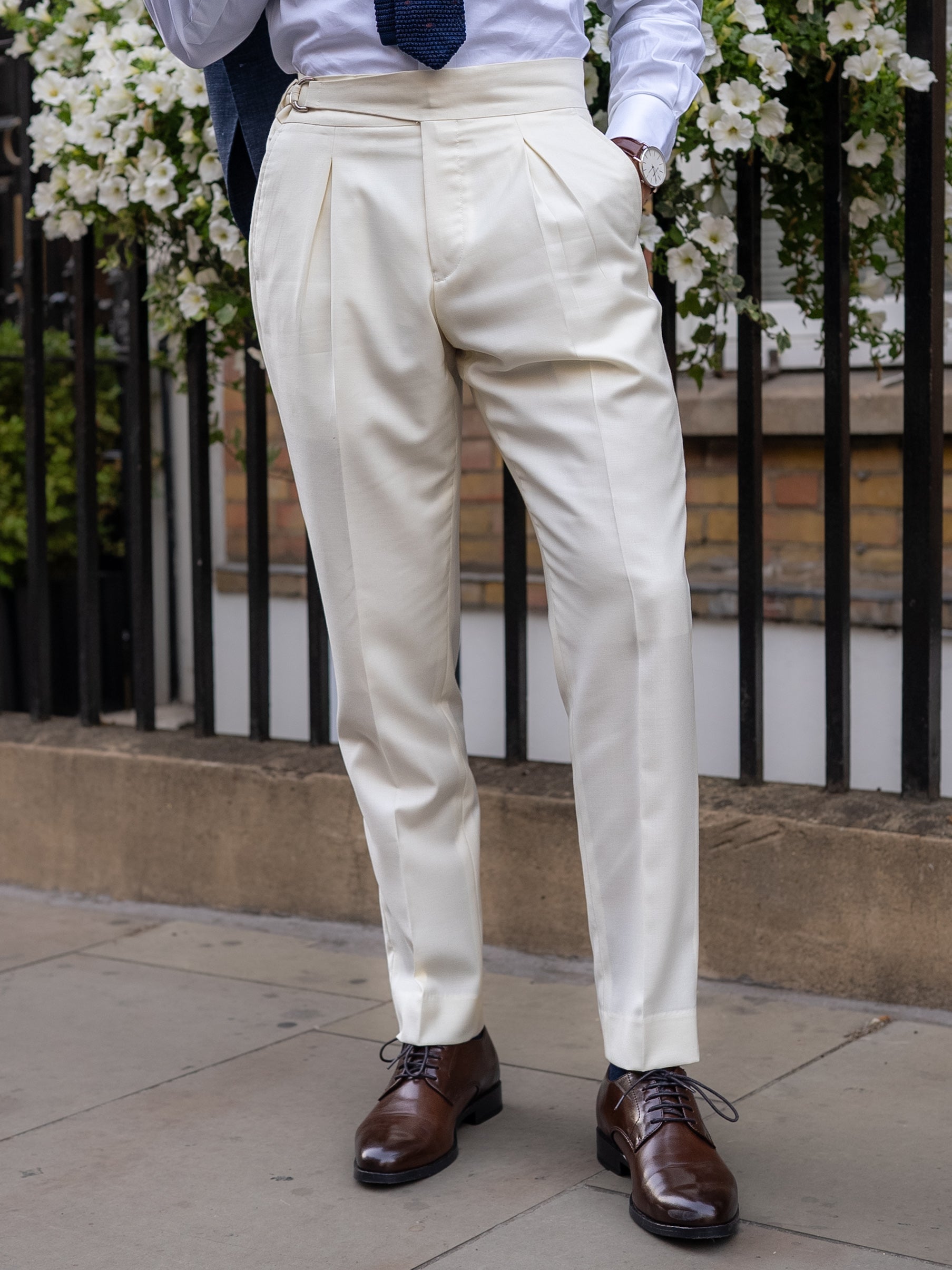 Front view of white tailored trousers, front pleats creating fluid drape and a composed shape, with a wide waistband and belt-free line for purity of form