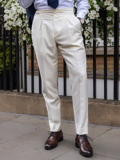 Front view of white tailored trousers, front pleats creating fluid drape and a composed shape, with a wide waistband and belt-free line for purity of form