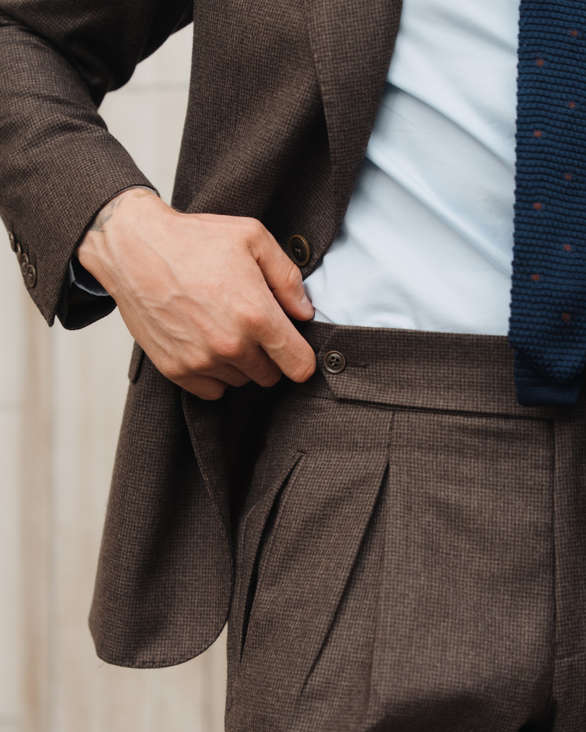Close-up of the man hold his trousers showing side fasteners on deep brown houndstooth trousers silhouette.